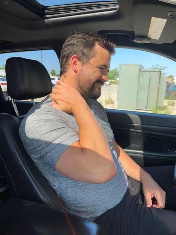 Waukee chiropractor demonstrating car seat stretch for neck and low back pain relief during road trips